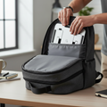 Person placing a laptop into a gray backpack on a desk.